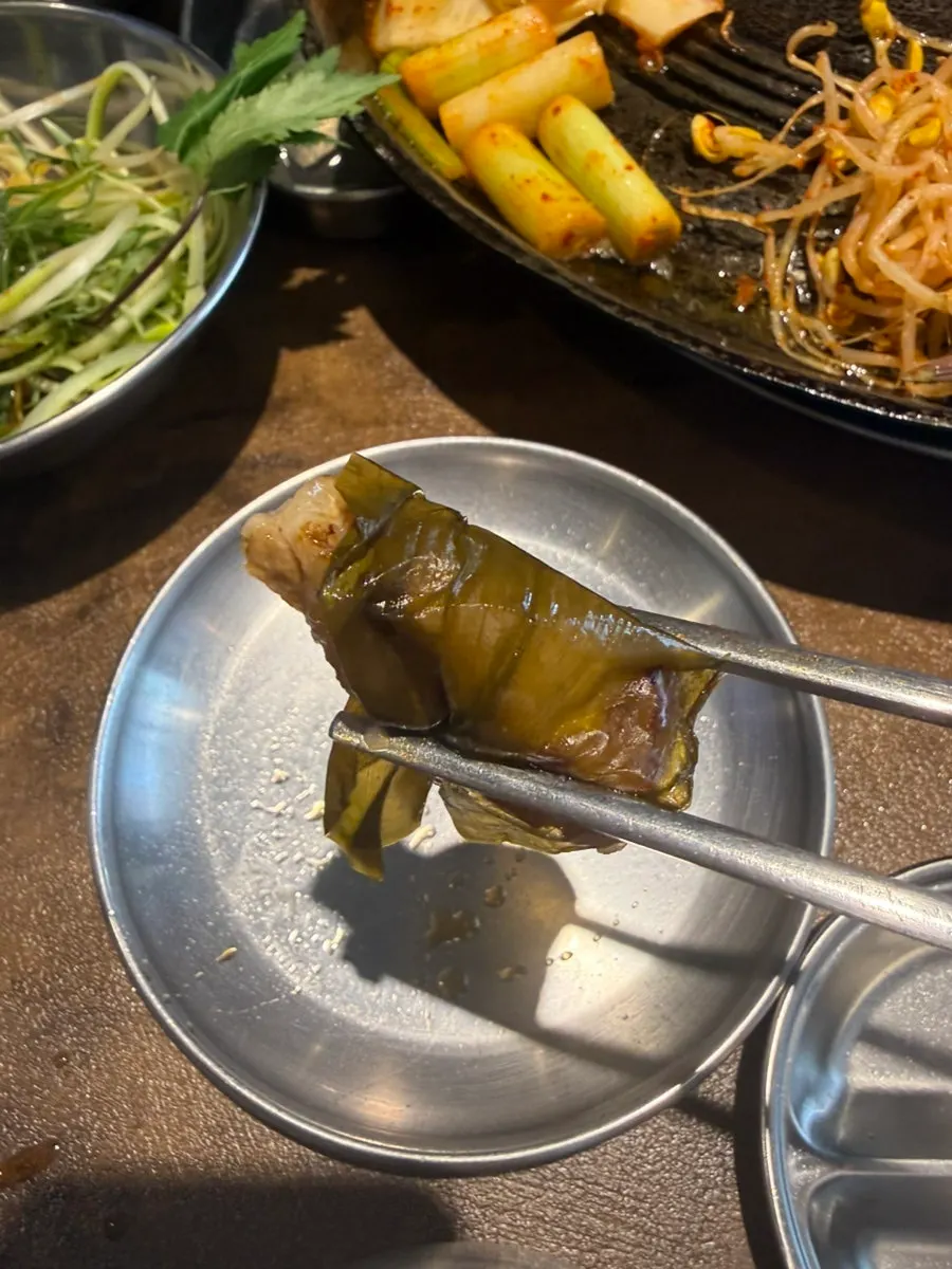 A grilled piece of pork belly picked up with tongs