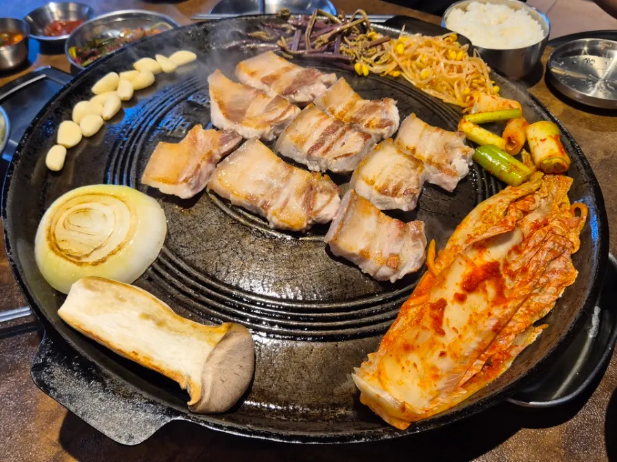 Pork belly and vegetables being grilled together on the cauldron lid
