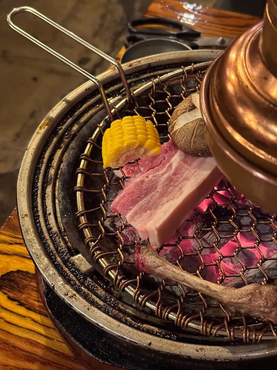 Pork belly grilling alongside corn and mushrooms