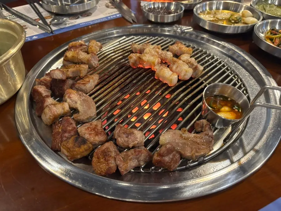 Pre-seared meat finishing on the grill next to salted anchovy sauce