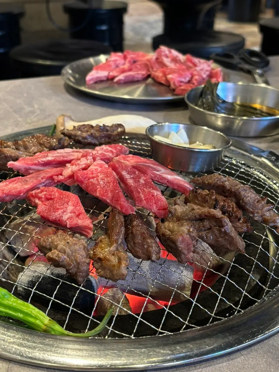 Grilled meat pushed to the side with raw meat freshly added