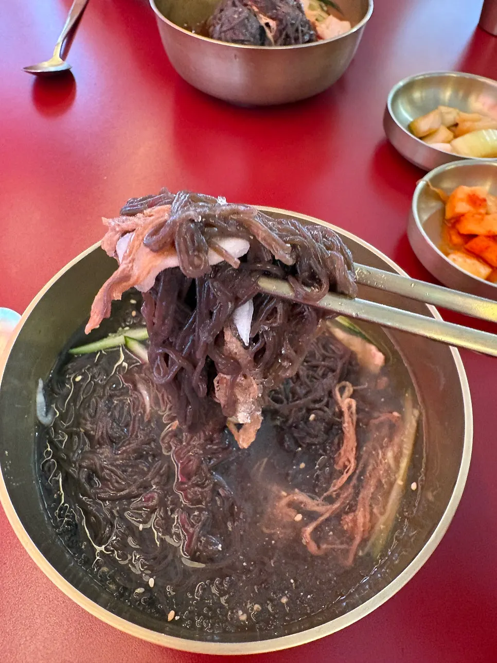Close-up of naengmyeon noodles being lifted with chopsticks