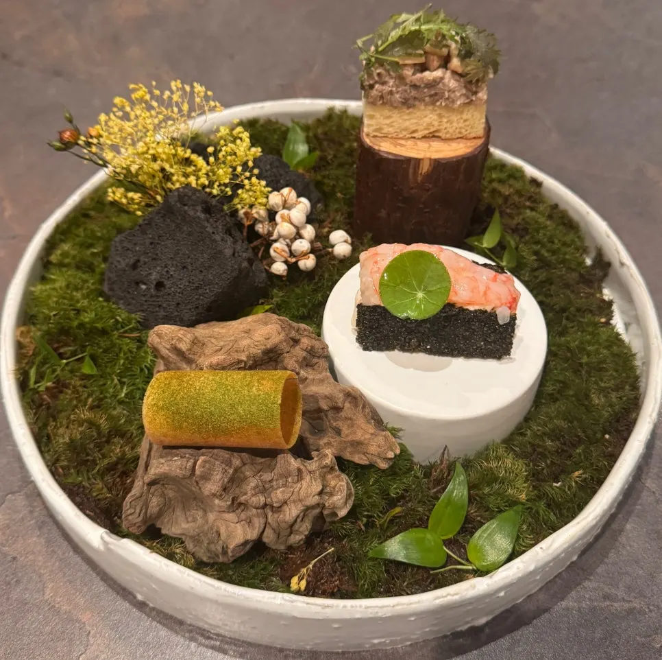 Three bite-sized dishes plated on a dish decorated with moss and stones