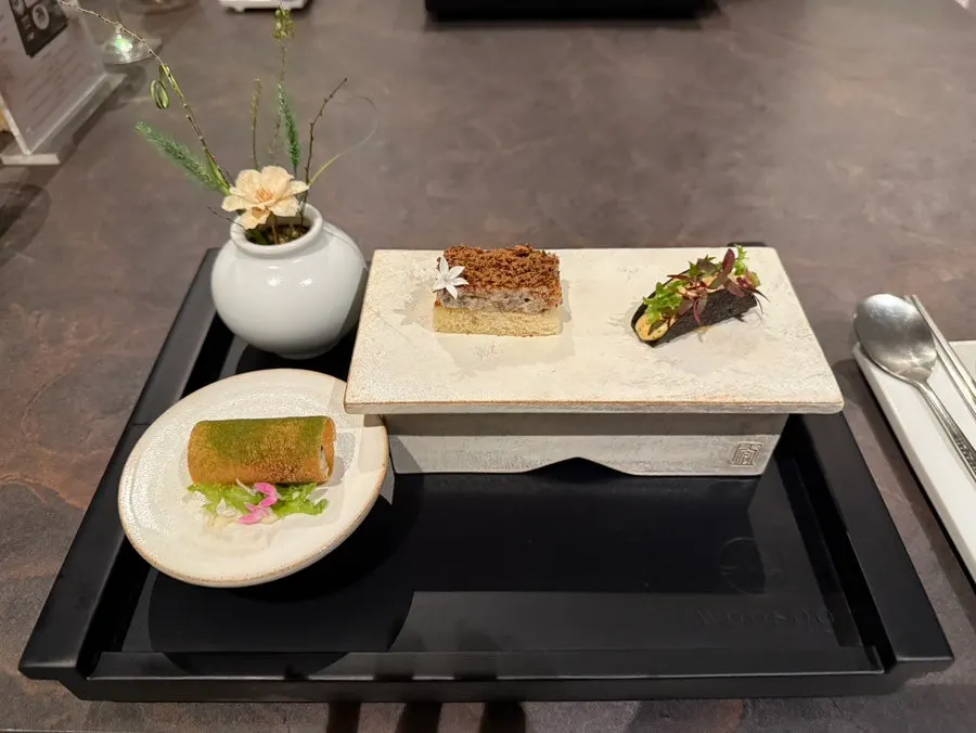 Three bite-sized dishes plated on moss and volcanic rock