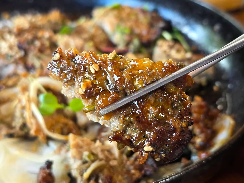 A piece of minari tteokgalbi coated in sauce