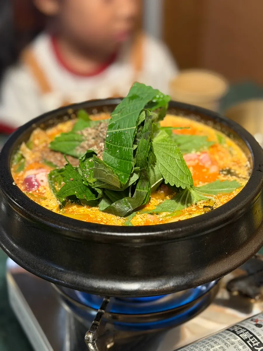 Earthenware pot of duck stew topped with perilla powder and sesame leaf