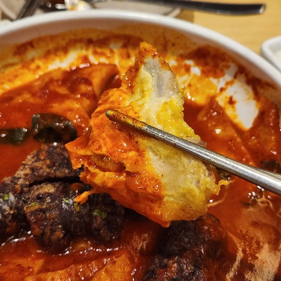 Yukjeon being dipped into tteokbokki sauce
