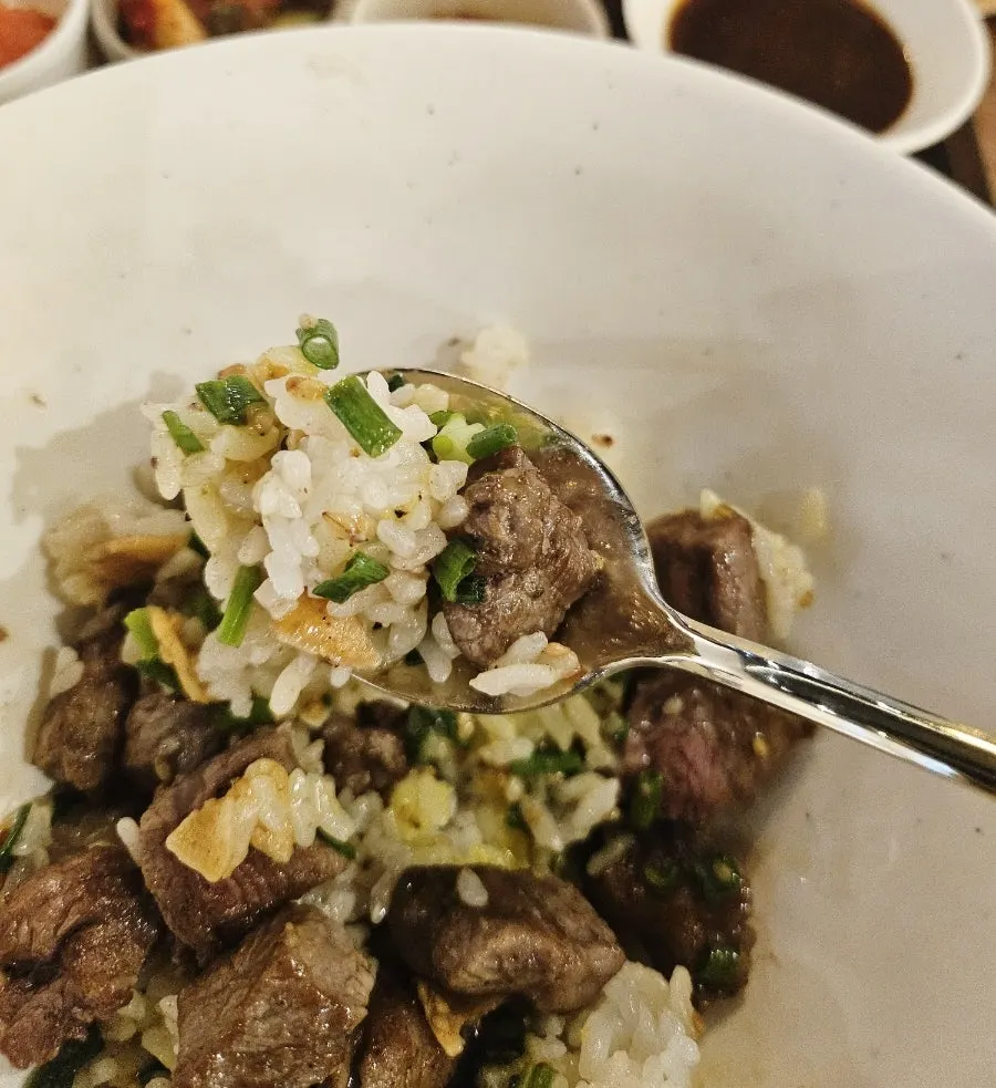 A spoonful of steak sotbap topped with side dishes