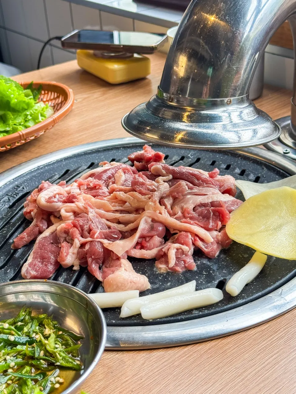 Raw duck on the grill next to simmering marinated duck