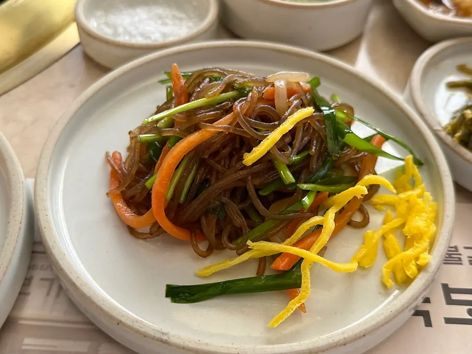 Side dish spread at Gukbo Garden including japchae, kimchi, and pajeori
