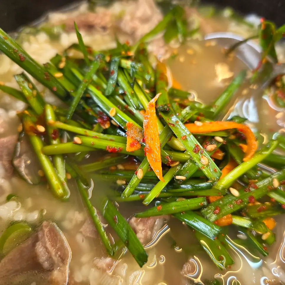 A spoonful of soup topped with chives and kkakdugi