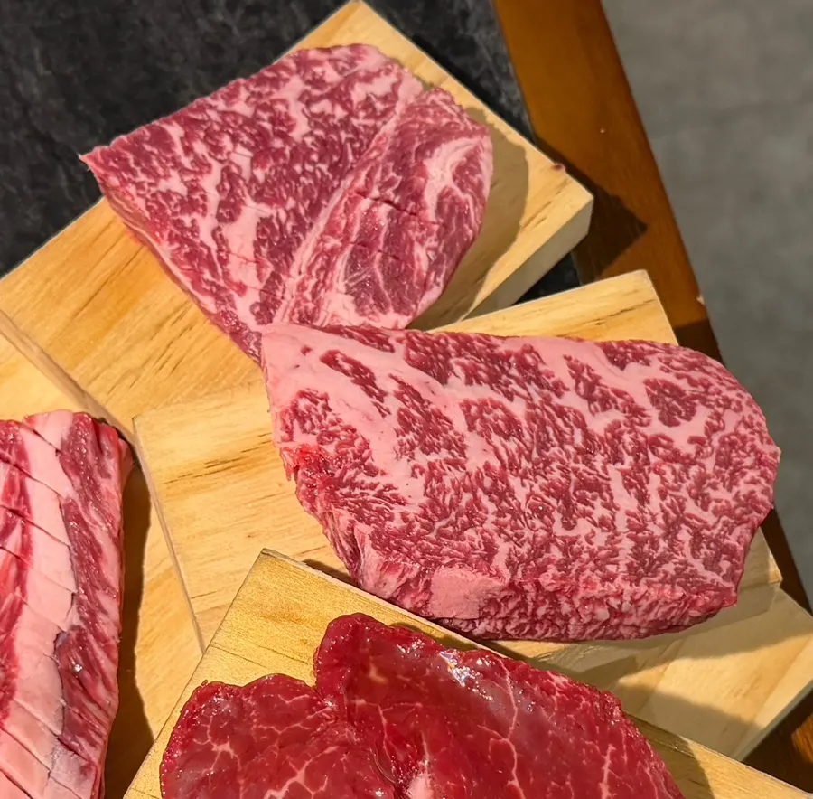 Assorted hanwoo cuts stacked on a wooden board with stamped king oyster mushrooms
