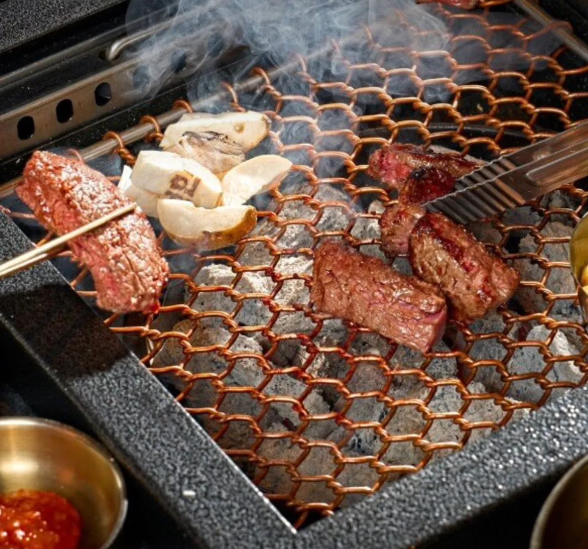 Hanwoo grilling over charcoal with smoke rising