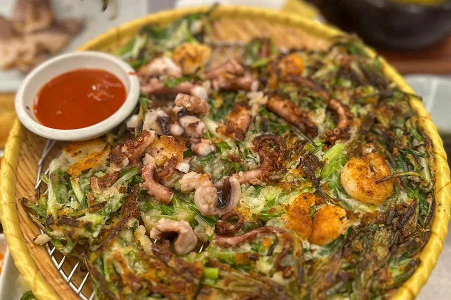 A piece of seafood pancake dipped in vinegar-chili sauce and soy sauce