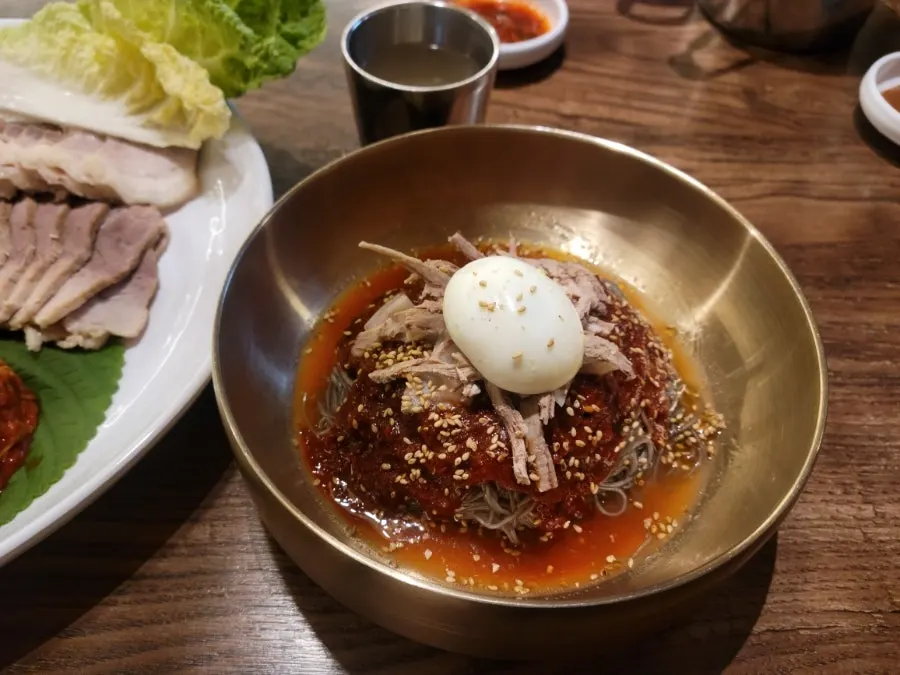Chewy naengmyeon noodles lifted with chopsticks