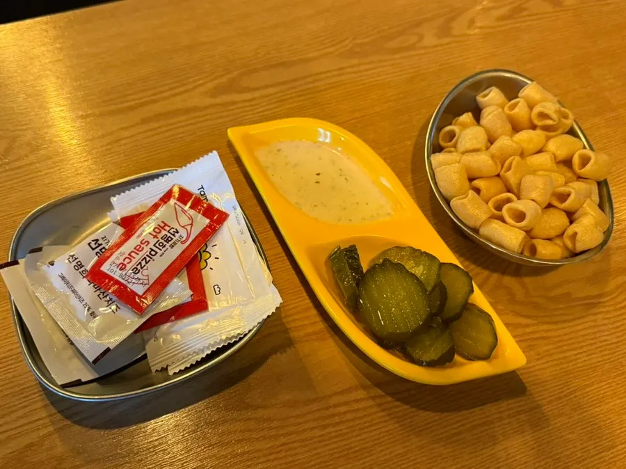 Garlic dipping sauce, pickles, parmesan cheese, and hot sauce set on the table