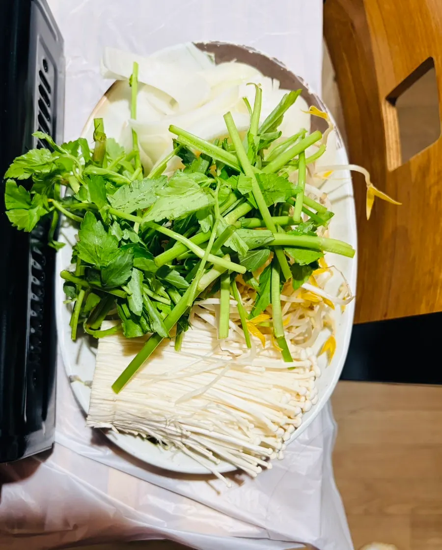 Griddle with beansprouts, minari and enoki mushrooms being stir-fried in