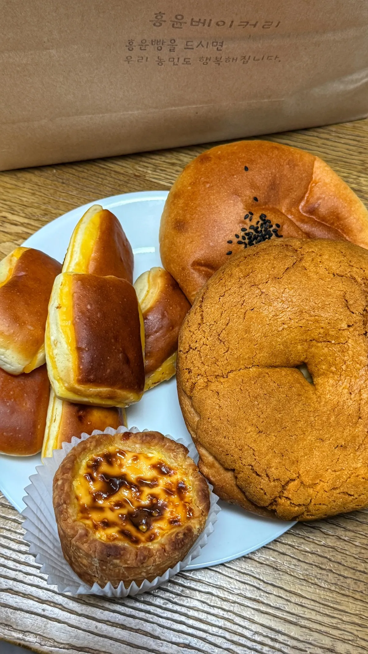 Plate with cheese bread, egg tart, sweet potato cream cheese bread, and chapssaltteok red bean bread