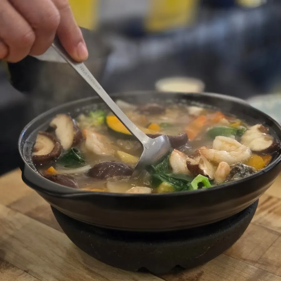Seafood sauce being poured over scorched rice in a stone bowl