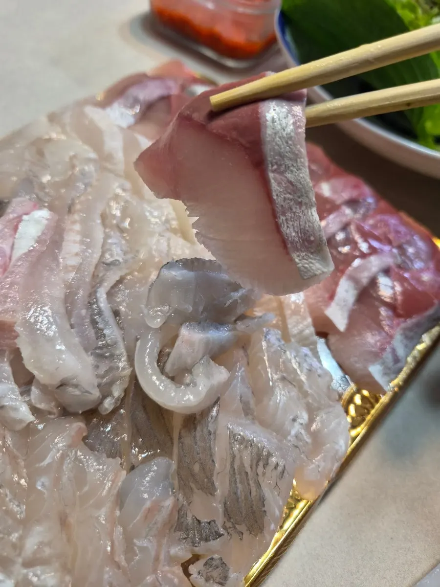 A piece of amberjack sashimi picked up with chopsticks