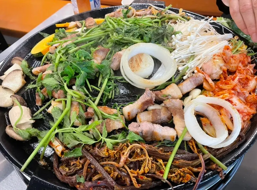 Meat, kimchi, and bracken fern cooking on the cast-iron lid