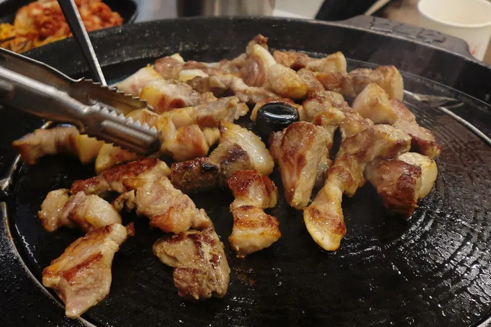 Pork jowl grilling on a pot lid