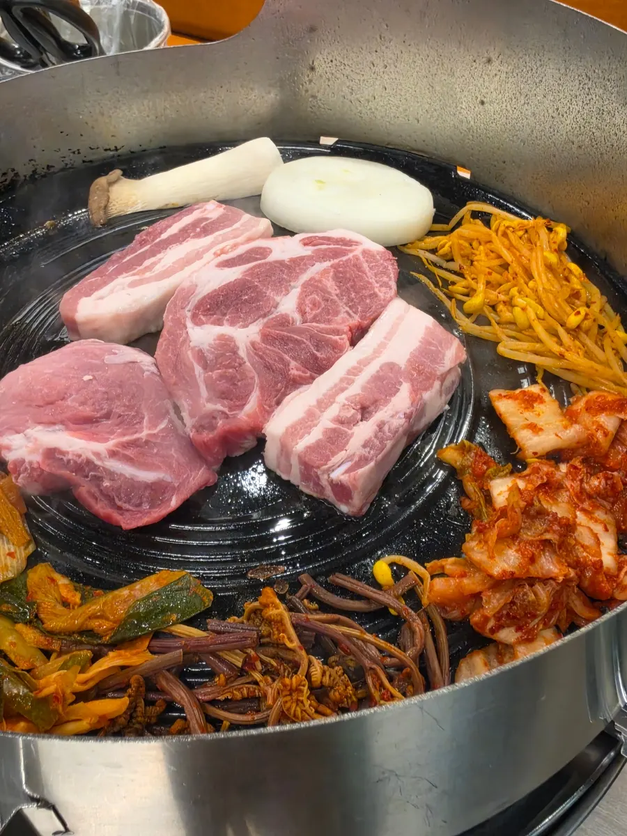 Pork belly with aged kimchi, bean sprouts, green onion kimchi and bracken fern on the cauldron-lid grill