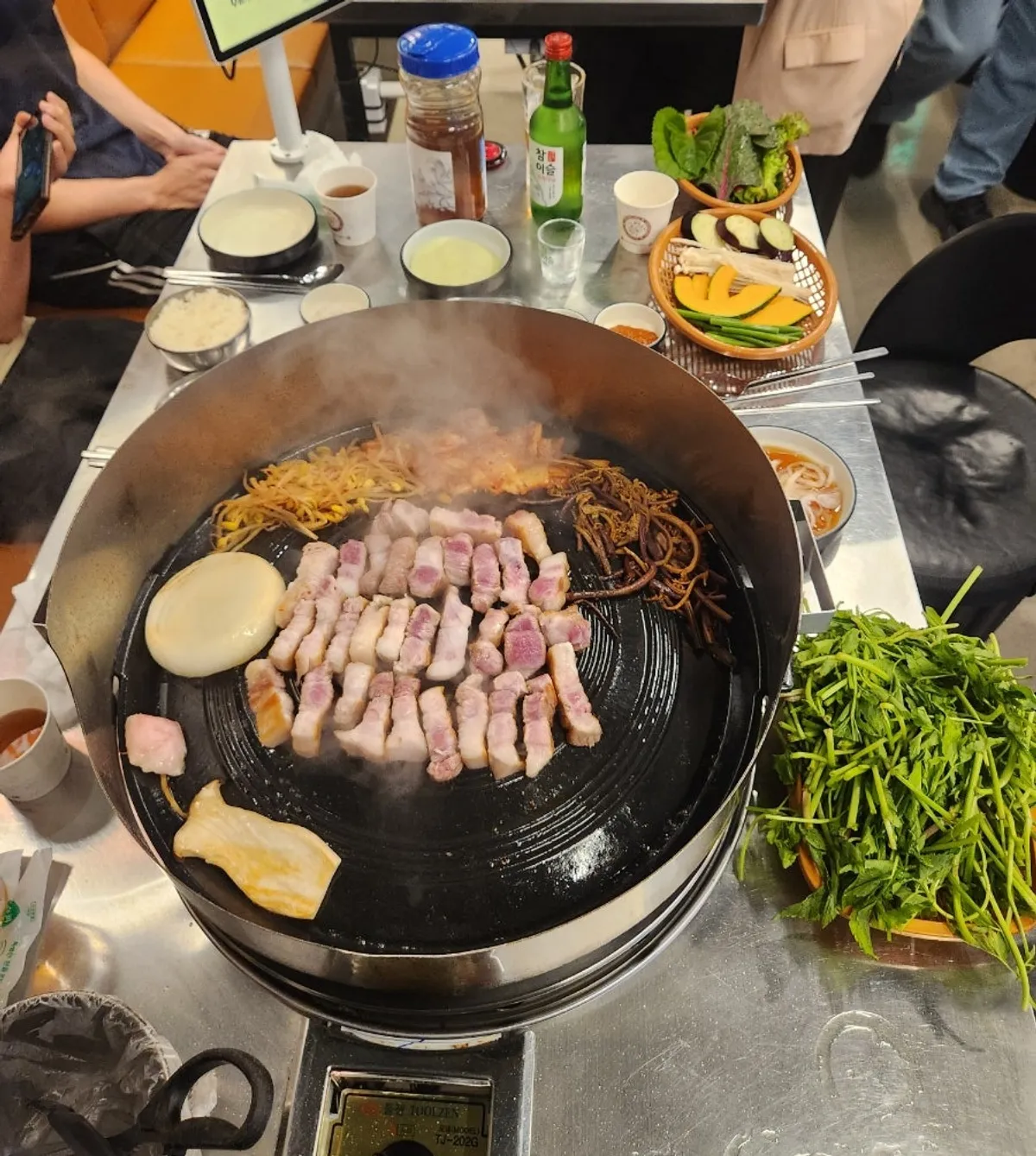 Pork belly and minari on the cauldron lid at Sanggu's Sotttukkeong Samgyeopsal Gueui Branch