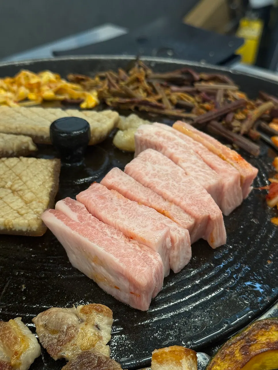 Pork jowl grilling on the iron lid