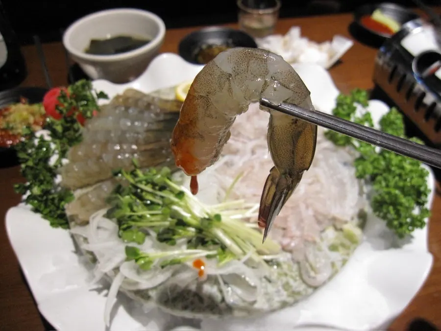 กุ้งดิบซาชิมิหนึ่งชิ้นที่หยิบขึ้นมาคลื่นใกล้ชิด