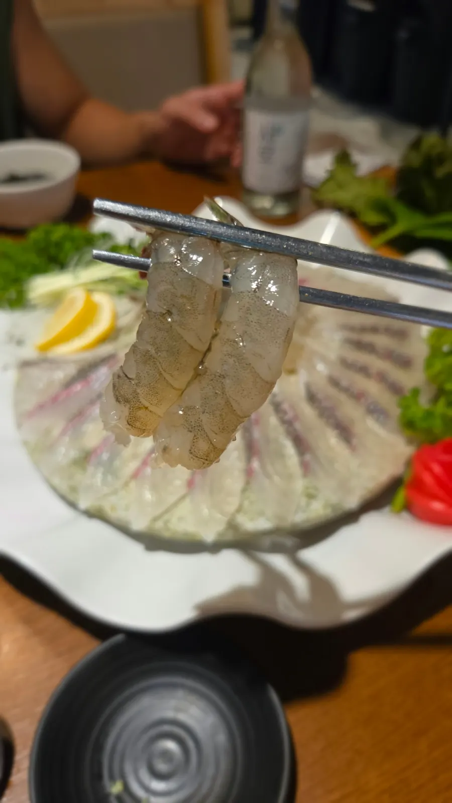 A firm piece of raw shrimp sashimi picked up with chopsticks