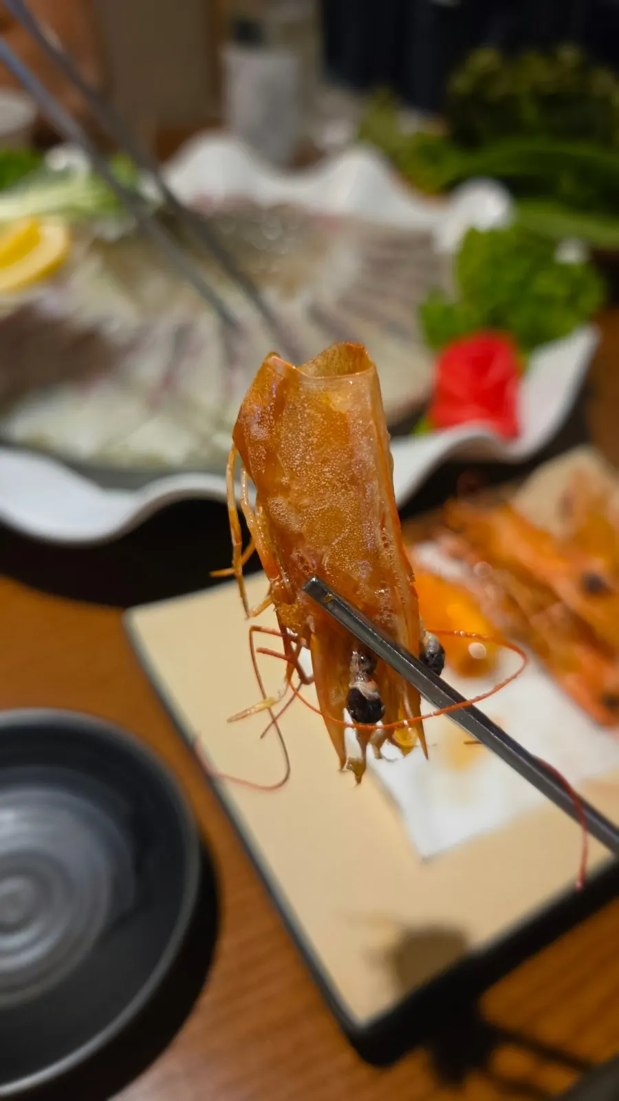 A piece of raw shrimp sashimi dipped in soy sauce