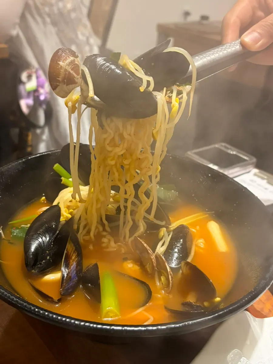 A pot of seafood ramyeon loaded with clams