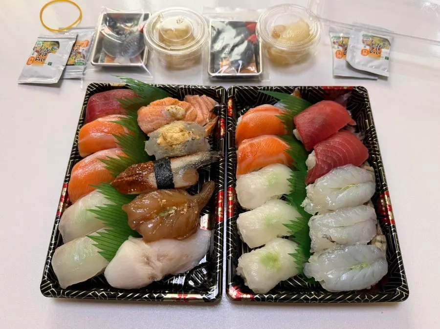 Two packed sushi boxes with a disposable soy sauce dish