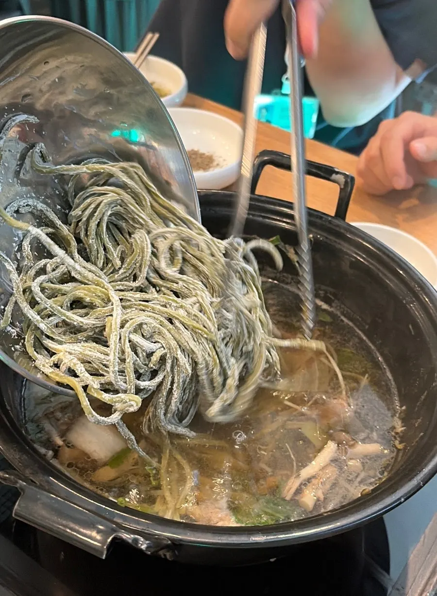Green-tinted kalguksu noodles cooked in the broth