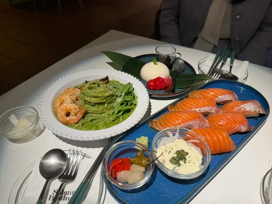 Table spread with raw salmon sushi and basil pesto pasta