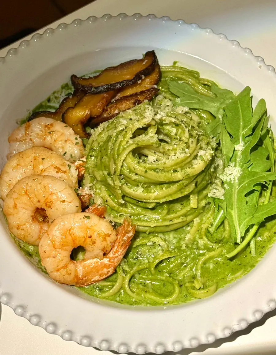 Basil pesto pasta topped with arugula, mushrooms, and shrimp