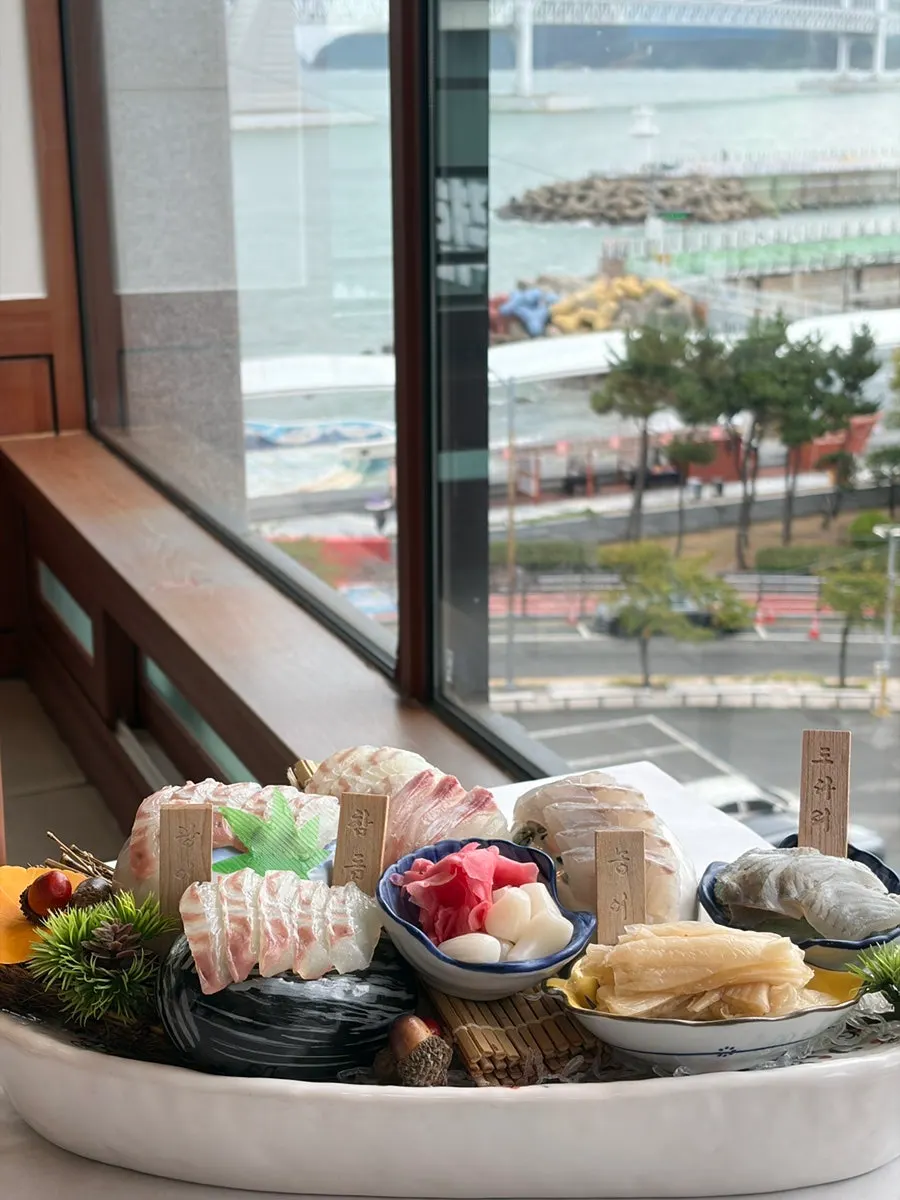 Mixed sashimi platter set against the Gwangalli sea backdrop