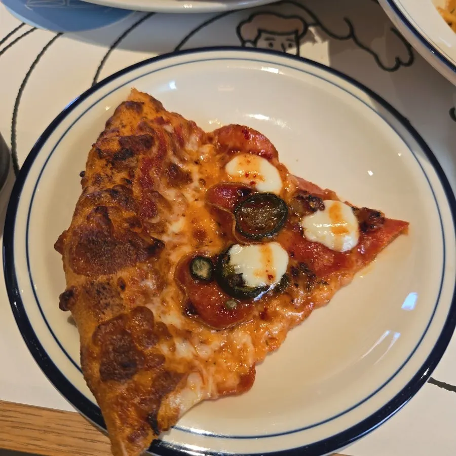 A slice of hot honey pepperoni pizza showing pickled chili