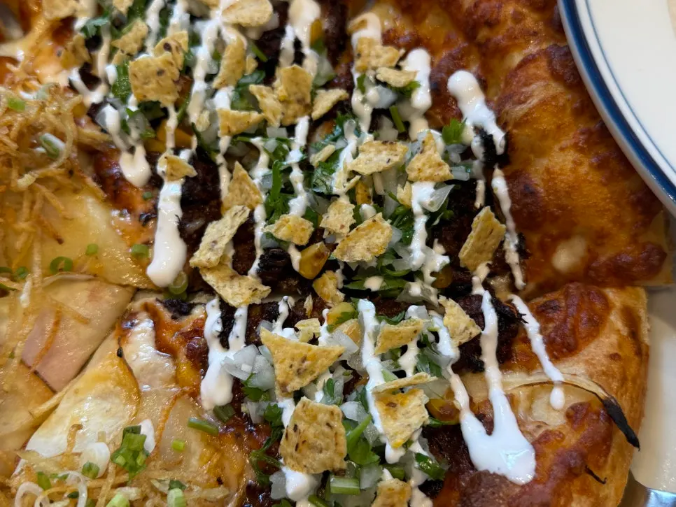 Pizza Birria Taco dengan keripik nacho dan ketumbar di atasnya