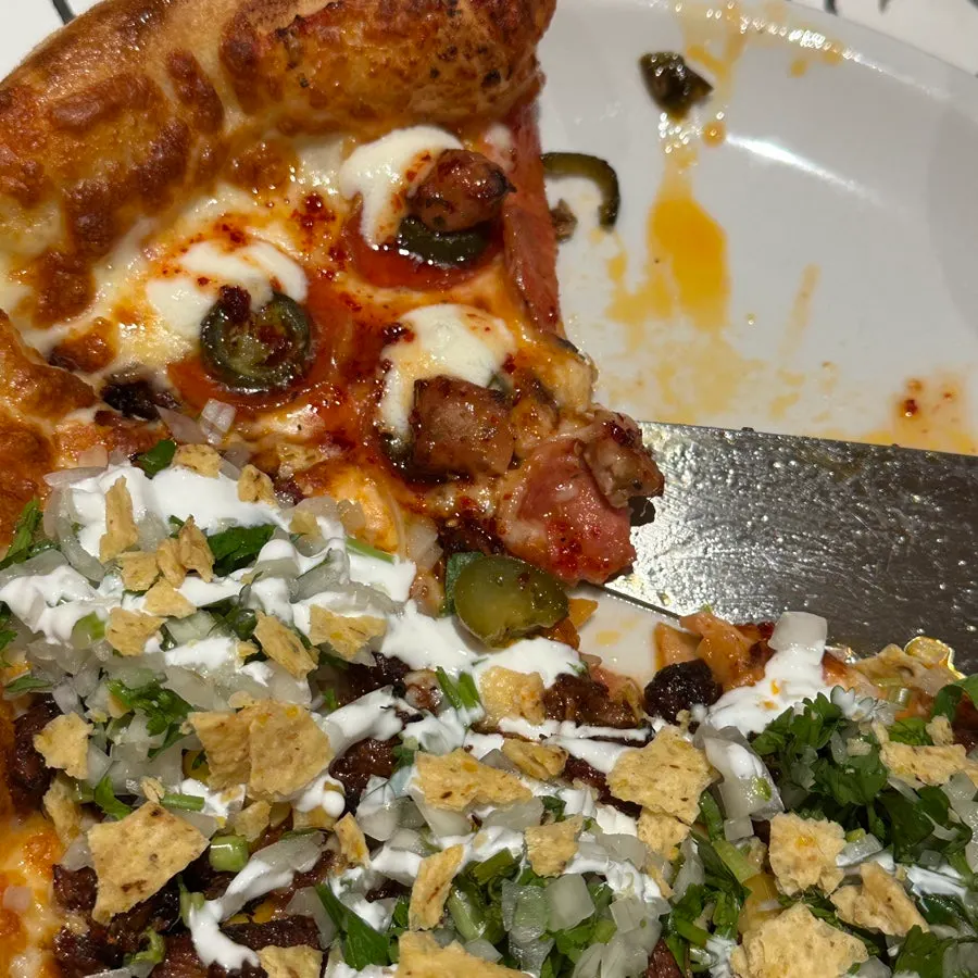Slice of birria taco pizza with sour cream