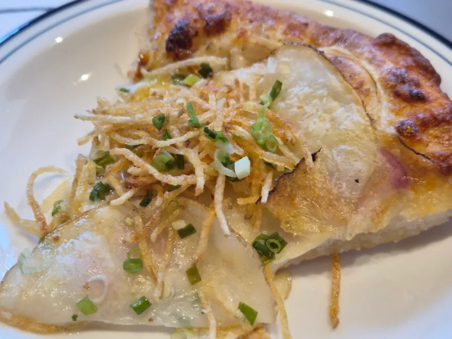 Slice of potato pizza topped with shredded potato