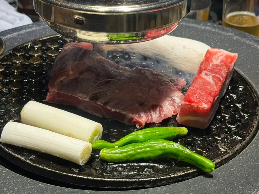 Meat, mushrooms, and green onion on the grill
