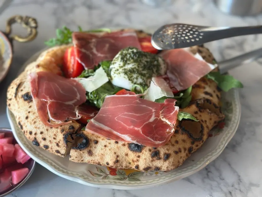 A slice of pizza topped with burrata and hamon