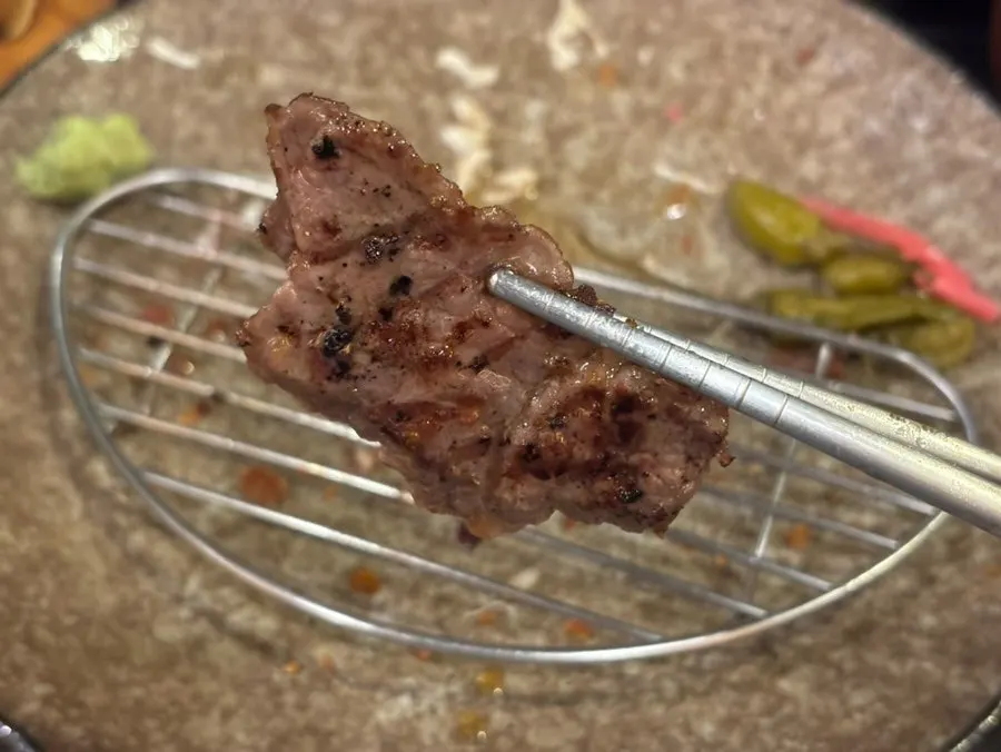 Grilled gyusteki being dipped into sauce