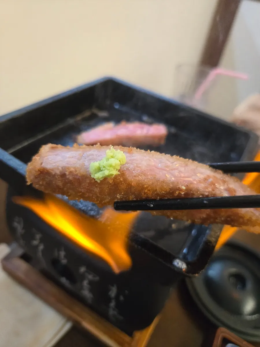 A piece of gyukatsu dipped in sauce with fresh wasabi on top