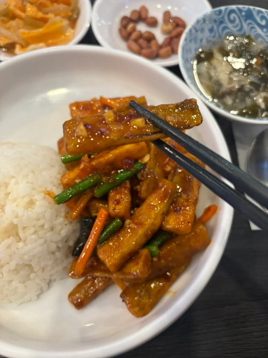 Lifting a piece of fried eggplant from the rice bowl