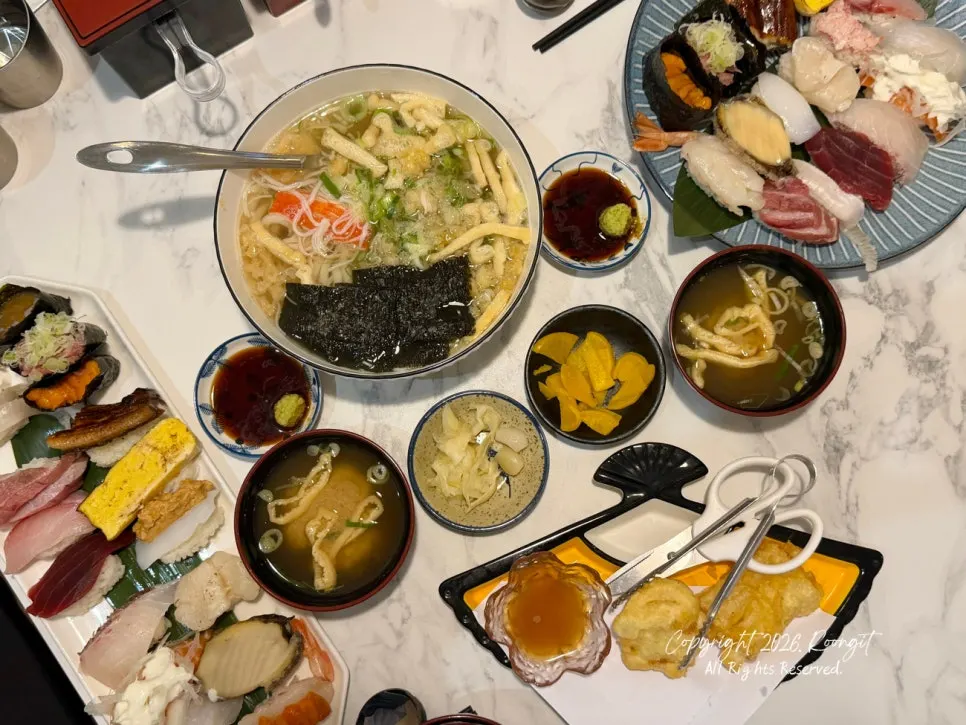 Sajian meja dengan sushi, udon, dan gorengan bersamaan