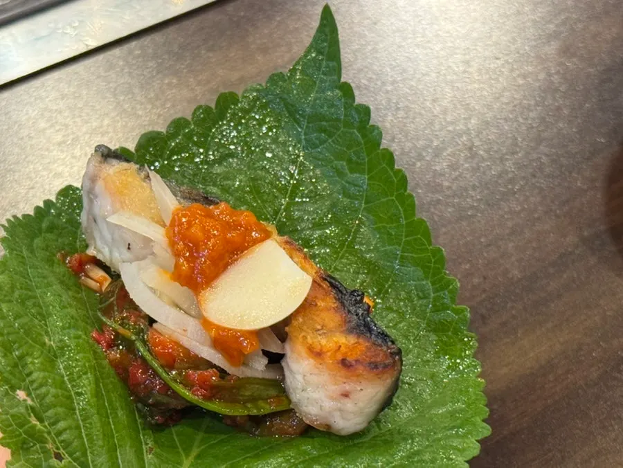 A piece of grilled eel topped with green onion kimchi and shredded ginger