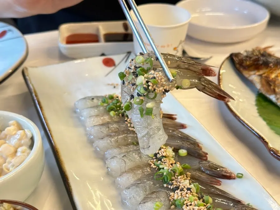 A piece of raw shrimp sashimi dipped in soy sauce